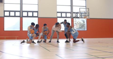 Diverse basketball team huddling with coach on court