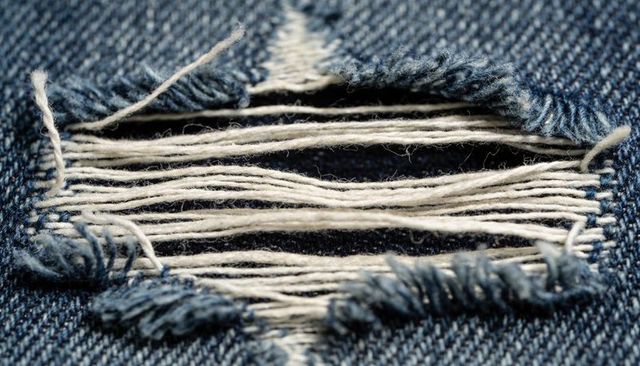 Macro view of ripped indigo denim revealing white weft threads and frayed blue warp