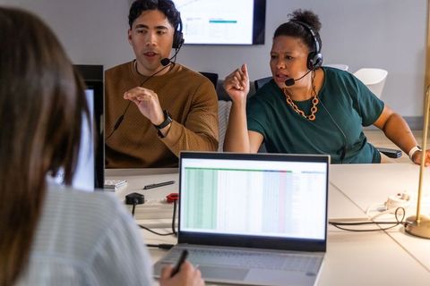 Customer support team collaborating over spreadsheet dashboard on laptops and headsets