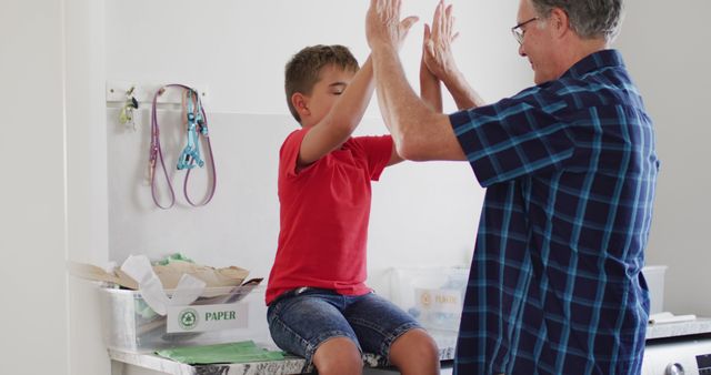 Happy doctor and young boy sharing a joyful high-five during healthcare examination in clinic. Young patient sitting on examination table with doctor engaging in friendly interaction. Perfect for healthcare themes, children's health services, and doctor-patient relationship promotions.