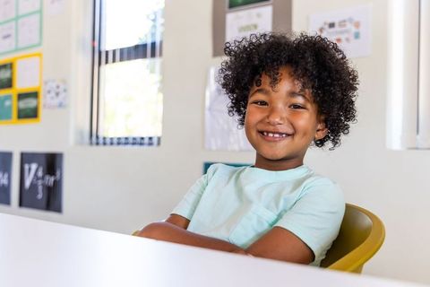 Smiling African American School-Aged Boy Sitting in Yellow Chair at Classroom Desk