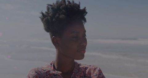 Contemplative woman standing at coastline closing eyes wearing patterned blouse