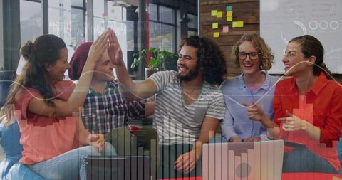 Young startup team celebrating success gathering around laptop with data dashboard overlay