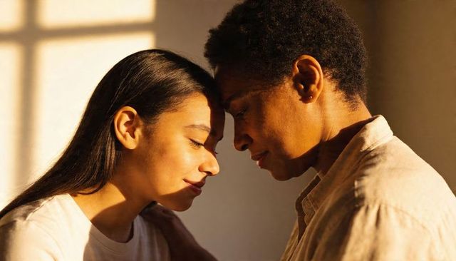 Sharing quiet comfort between two women leaning foreheads in warm sunlight