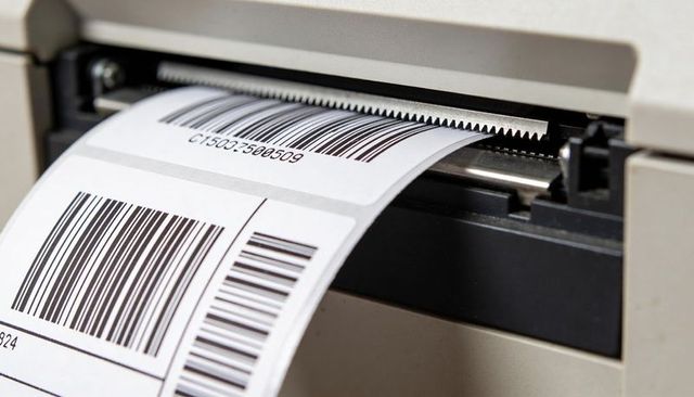 Thermal label printer feeding adhesive barcode labels for warehouse shipping and inventory
