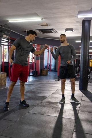 Two men fist-bumping after jump rope workout in crossfit gym, teamwork motivation