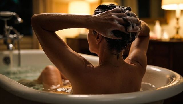 Washing hair in bathtub at night, cozy warm lighting and relaxing self-care ritual