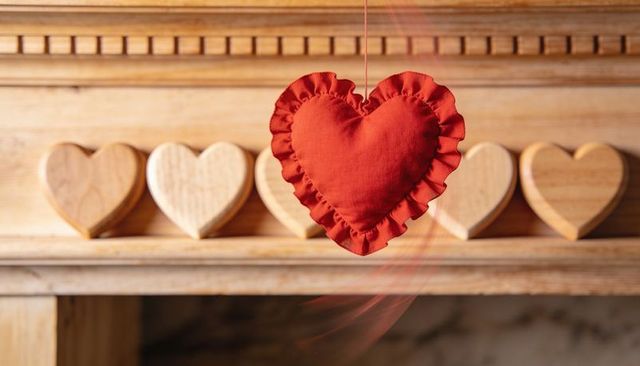 Hanging red ruffled fabric heart swaying before rustic wooden carved hearts on mantel