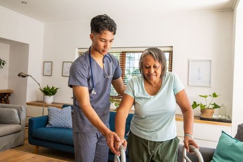 Hispanic nurse helping senior woman with walker at home for rehabilitation