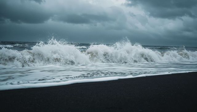 Storm waves crashing on black sand beach with white foam under moody sky