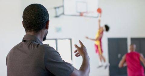 Basketball Coach Observes Players Practicing in Gym