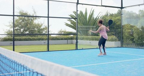 African american woman preparing forehand on blue padel court with glass enclosure