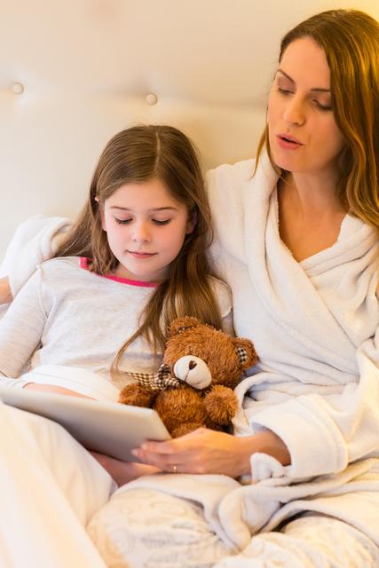 Mother and daughter bonding over a digital tablet in a cozy home setting, perfect for illustrating family togetherness, modern parenting, or technology use in family life. Ideal for use in advertising related to parenting tips, family life, or digital technology.