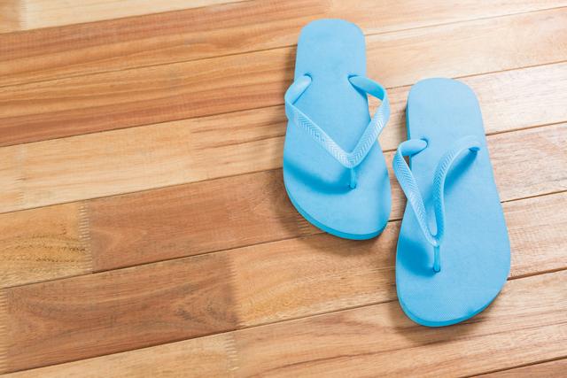 Blue flip flops placed on a wooden floor, evoking a sense of summer and relaxation. Ideal for use in travel blogs, vacation advertisements, summer fashion promotions, and lifestyle articles.