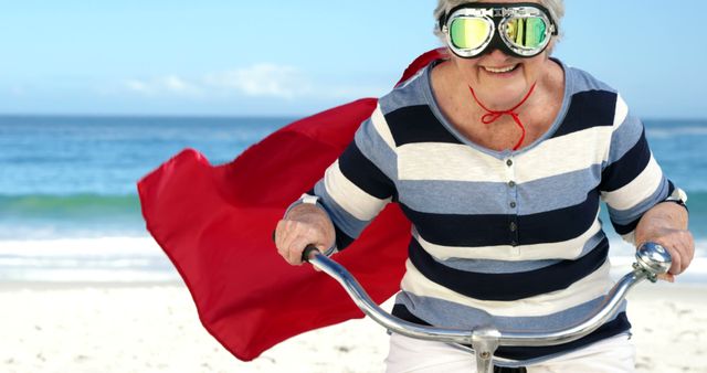 Senior Woman Wearing Goggles and Red Cape Riding Bicycle on Beach - Download Free Stock Images Pikwizard.com