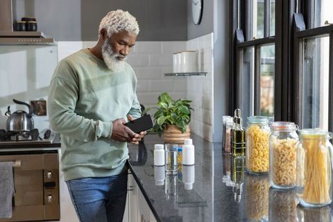 Senior African American man checking medication and using smartphone in modern kitchen