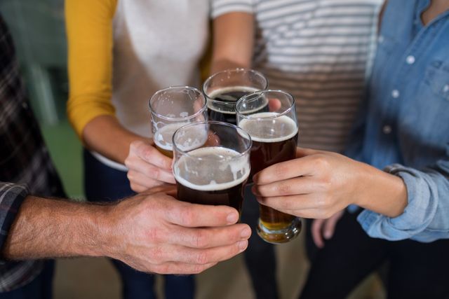 Group of friends raising beer glasses in a brewery, celebrating and enjoying time together. Perfect for use in advertisements for breweries, social events, and lifestyle blogs focusing on friendship and social gatherings.