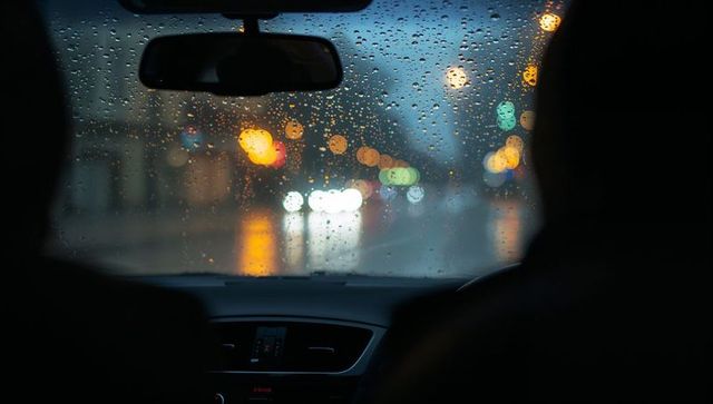 Rain-dappled windshield capturing city bokeh lights at night from rearview car interior