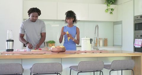 African american couple preparing fresh fruit on modern kitchen island, healthy lifestyle
