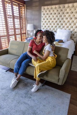 Sunlit bedroom moment: diverse female couple sharing affectionate embrace on sofa
