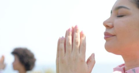 Women practicing meditation on beach, closing eyes and pressing hands in prayer pose