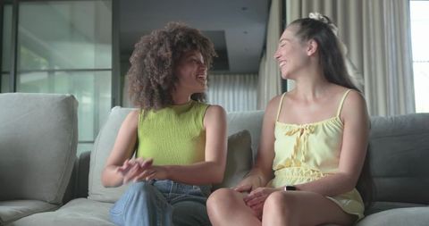 Friends laughing and chatting on sofa in modern home wearing green and yellow summer outfits