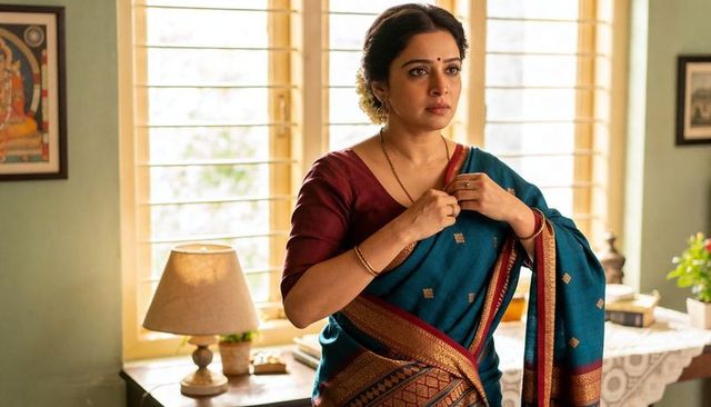 Adjusting necklace, indian woman in teal saree and maroon blouse near slatted window