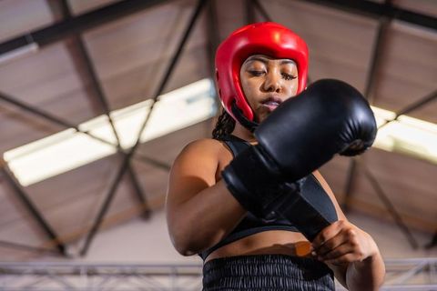 Focused african american boxer adjusting glove and headguard during intense gym training