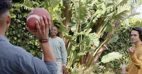 Diverse friends playing backyard football among tropical plants, casual summer hangout