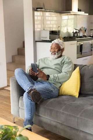 Senior african american man relaxing on sofa and using smartphone in modern kitchen