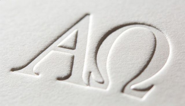 Embossed alpha and omega letters pressing into textured paper macro detail