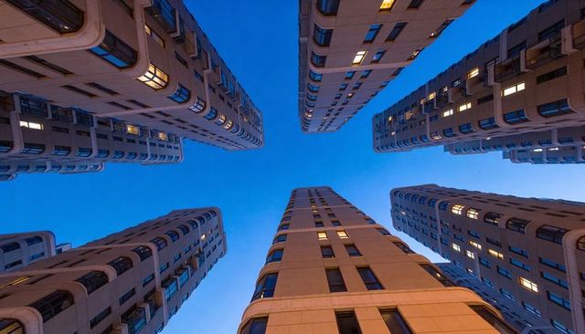 High-rise towers converging above narrow courtyard at dusk with glowing bay windows