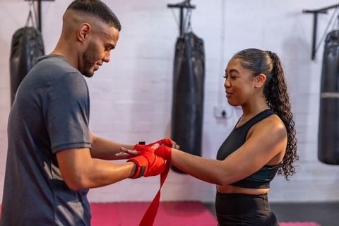 Boxing coach wrapping red hand wraps for female trainee during gym training session