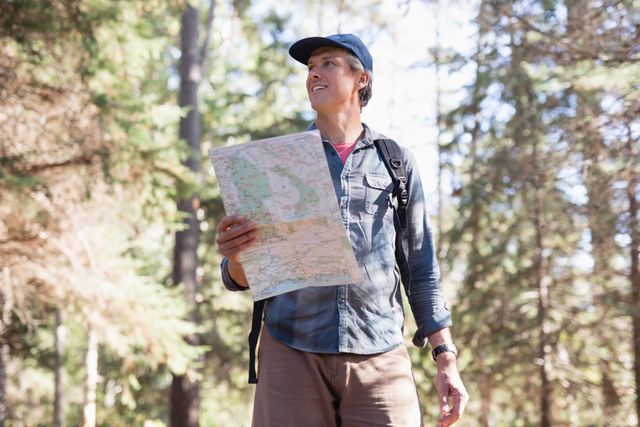 Low angle view of mature male hiker with map standing in forest
