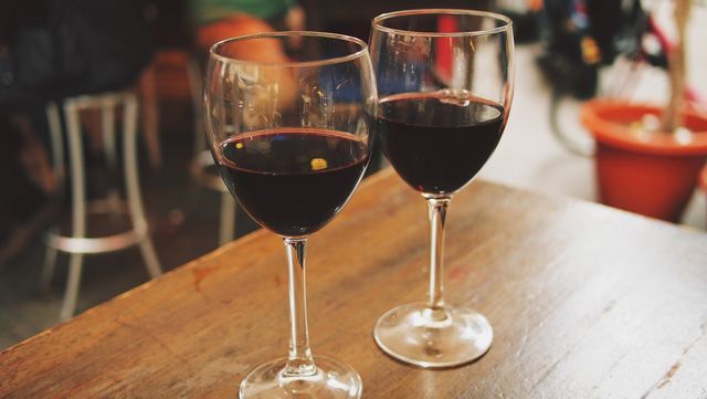 Two glasses of red wine are placed on a wooden table, evoking a sense of intimacy and coziness. Ideal for use in articles or advertisements related to wine tasting, bars, romantic evenings, celebrations, or relaxation.