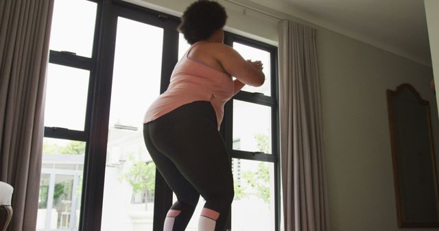 Woman doing a workout in front of large windows at home. Use for fitness blogs, healthy living articles, and workout tutorials.