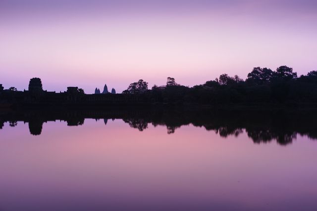 Silhouette of trees and structures reflected in calm water during a serene dusk creates a tranquil mood perfect for depicting stillness, peacefulness, and the beauty of nature. Ideal for use in travel brochures, meditation apps, and websites related to relaxation and nature.