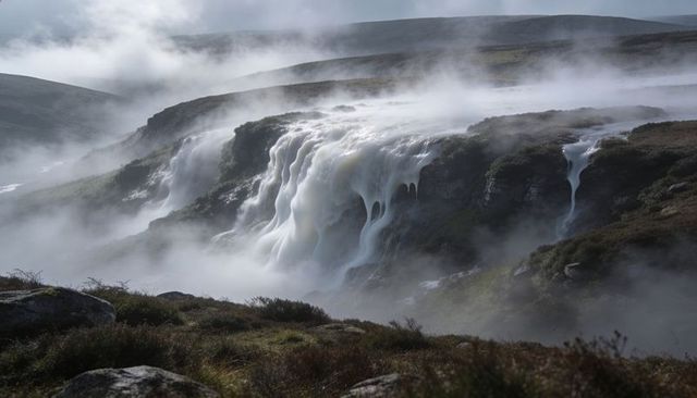 Misty highland waterfall cascading over rocky escarpment on moorland plateau