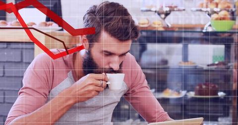 Bearded man sipping espresso while working on laptop in bakery with pastry display