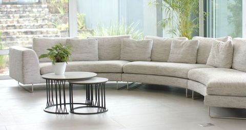 Light-gray curved sectional sofa with nesting tables and plant in modern glass lounge