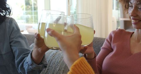 Sunlit friends toasting with lemonade on sofa, cozy casual gathering, smiling trio