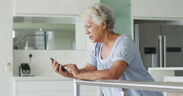 This image features an African American senior woman happily using her smartphone at home during lockdown. This can be used in articles or advertisements on senior lifestyle, retirement, staying connected through technology, or life during quarantine. It also suits content about family communication, elderly independence, or mobile app usability for older adults.