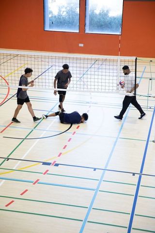 African american teen volleyball team training with coach in indoor gymnasium
