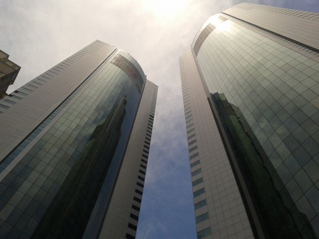 View of two modern twin skyscrapers reflecting the sky and sunlight, emphasizing their height and sleek glass facades. This image is ideal for use in presentations, corporate websites, real estate materials, urban development promotions, and more, highlighting urban life and modern architecture.