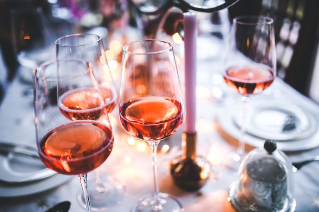 Several wine glasses filled with rose wine showcased on an elegant dinner table illuminated by candlelight. This image conveys a sense of sophistication, romance, and festivities — suitable for content related to fine dining, romantic dinners, special occasions, and celebrations.