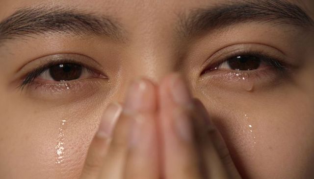 Crying asian woman pressing hands over mouth in intimate extreme close-up headshot