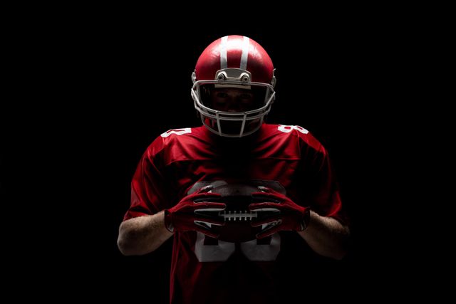 American football player standing with rugby helmet and ball against black background. Strong American Football Player concept for Championship Football Tournament