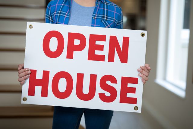 Person holding open house sign in a living room, ideal for real estate promotions, property listings, and open house event advertisements.