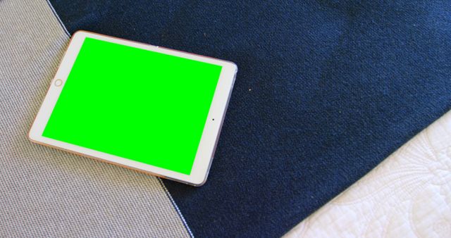 Digital tablet features a vibrant green screen perfect for adding custom content. Lying on a surface with dark cloth, perfect for showcasing app designs, multimedia creativity, or educational usage. Ideal for use in technology and home lifestyle contexts.