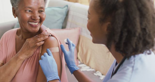 Shows a caring nurse giving a flu shot to a senior woman who is smiling. Ideal for healthcare-related materials, promoting immunization and preventive care services. Demonstrates trust, healthcare at home, and positivity in a medical context.